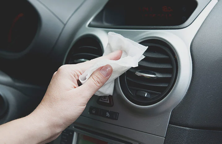 Hand reinigt Lüftungsschlitz im Auto mit Tuch